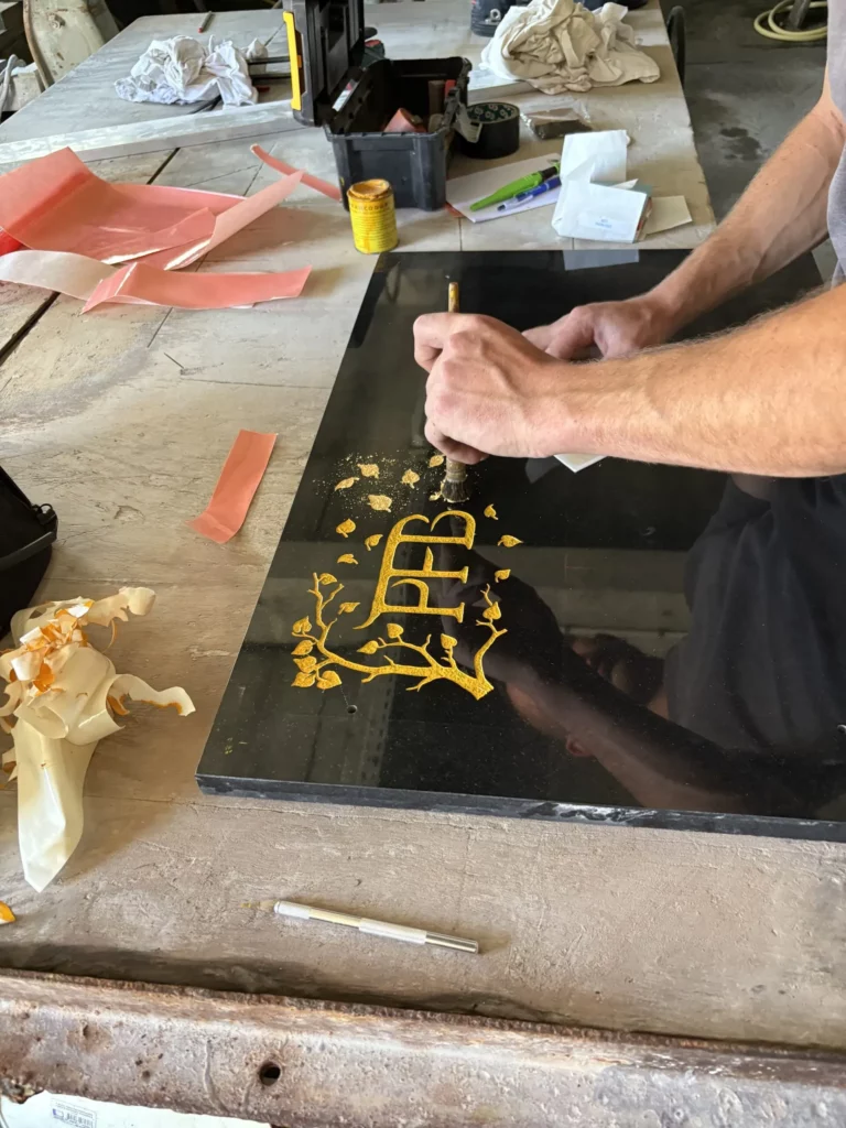 Artisan dorant un logo PFB à la feuille d'or sur une plaque de granit noir poli.