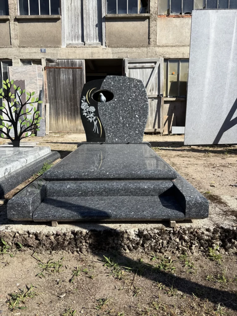 Pierre tombale en granit noir poli avec sculpture de fleurs et fenêtre au centre.